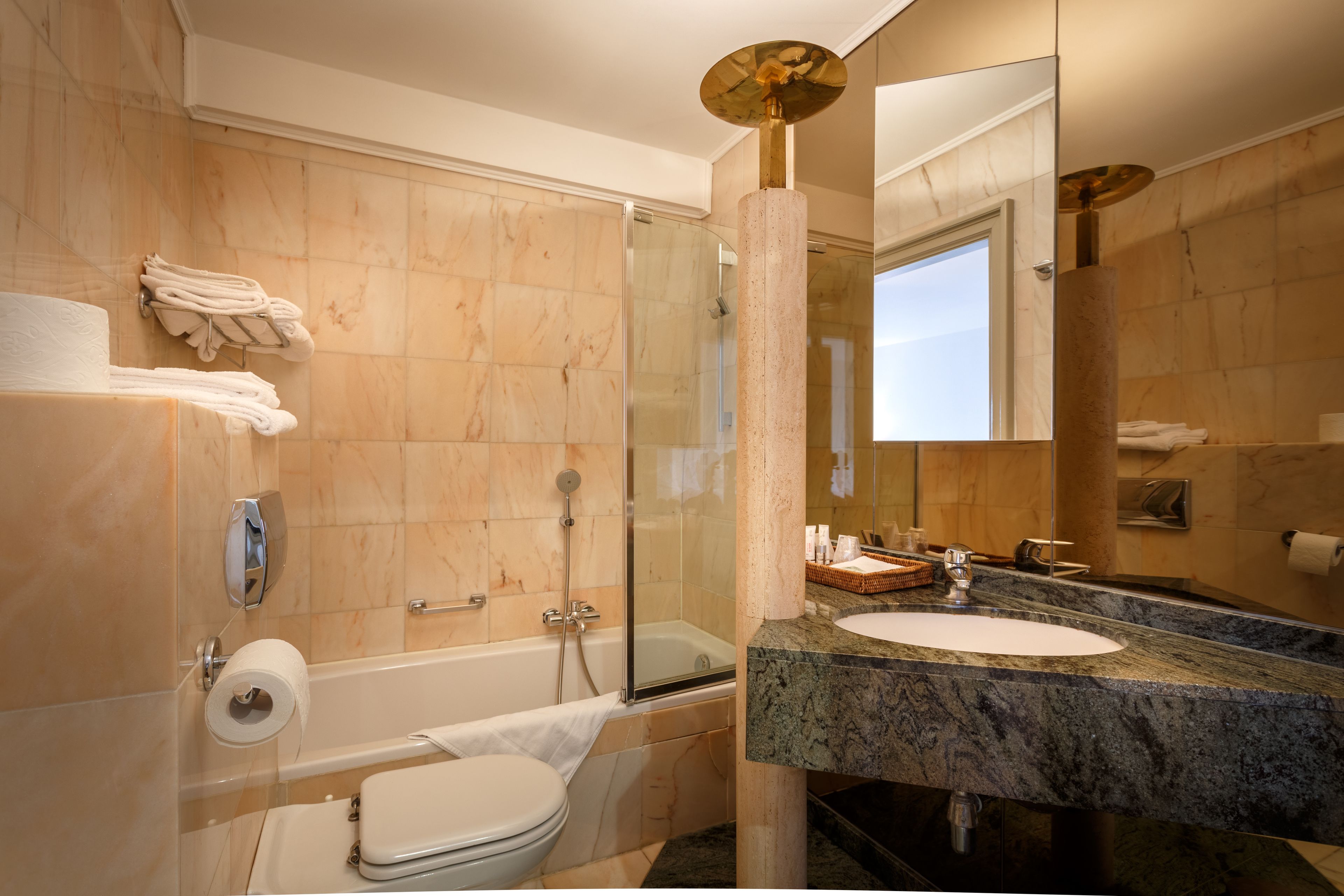 A modern bathroom with a glass-enclosed shower, a bathtub, a toilet, and a sink with a marble countertop.
