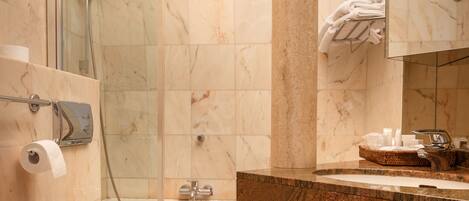Un baño moderno con cabina de ducha de vidrio, pared con azulejos de mármol, una columna central, lavamanos con encimera de mármol y un inodoro.