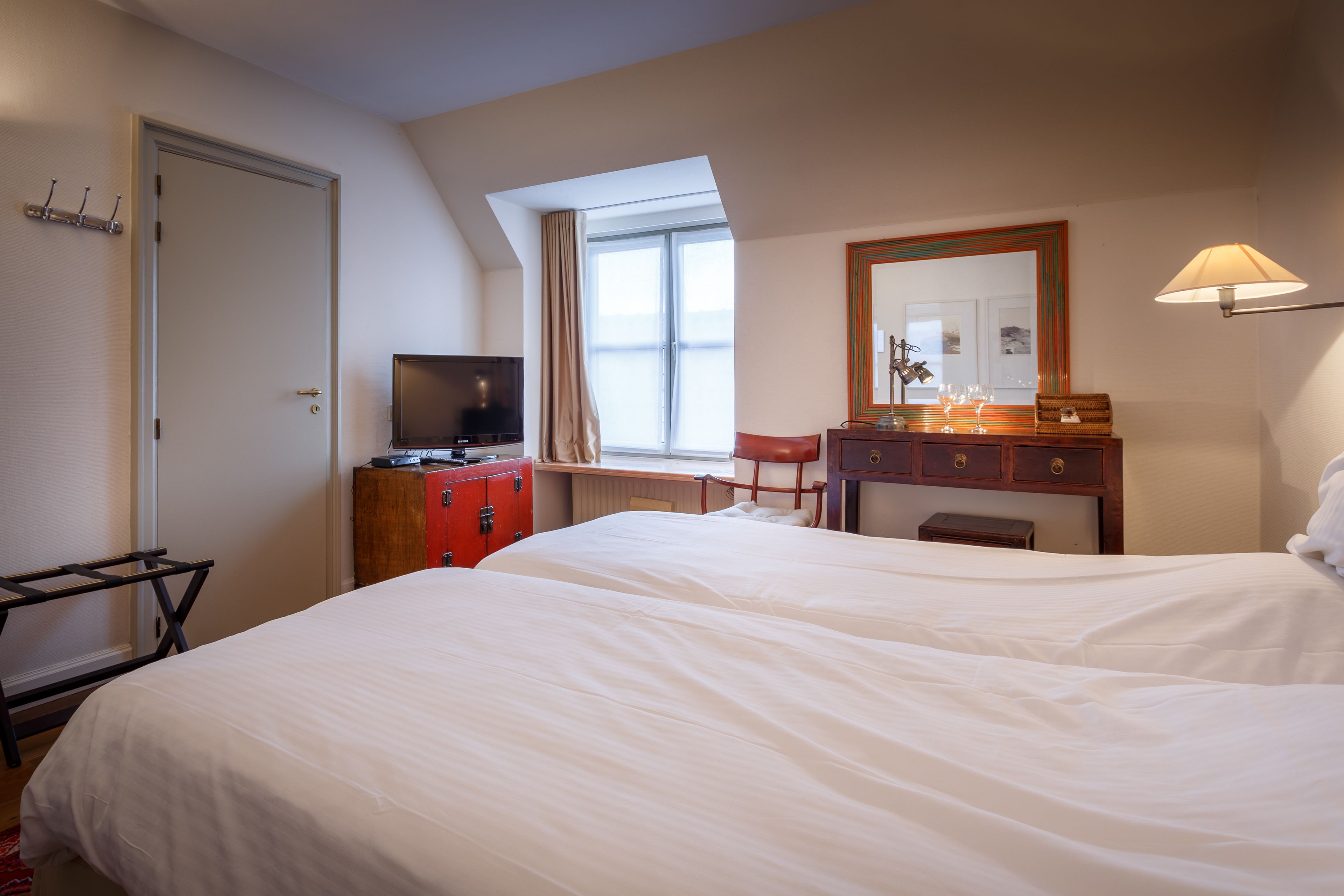 Una habitación de hotel con una cama grande, un televisor, un escritorio con lámpara y una ventana con cortinas.