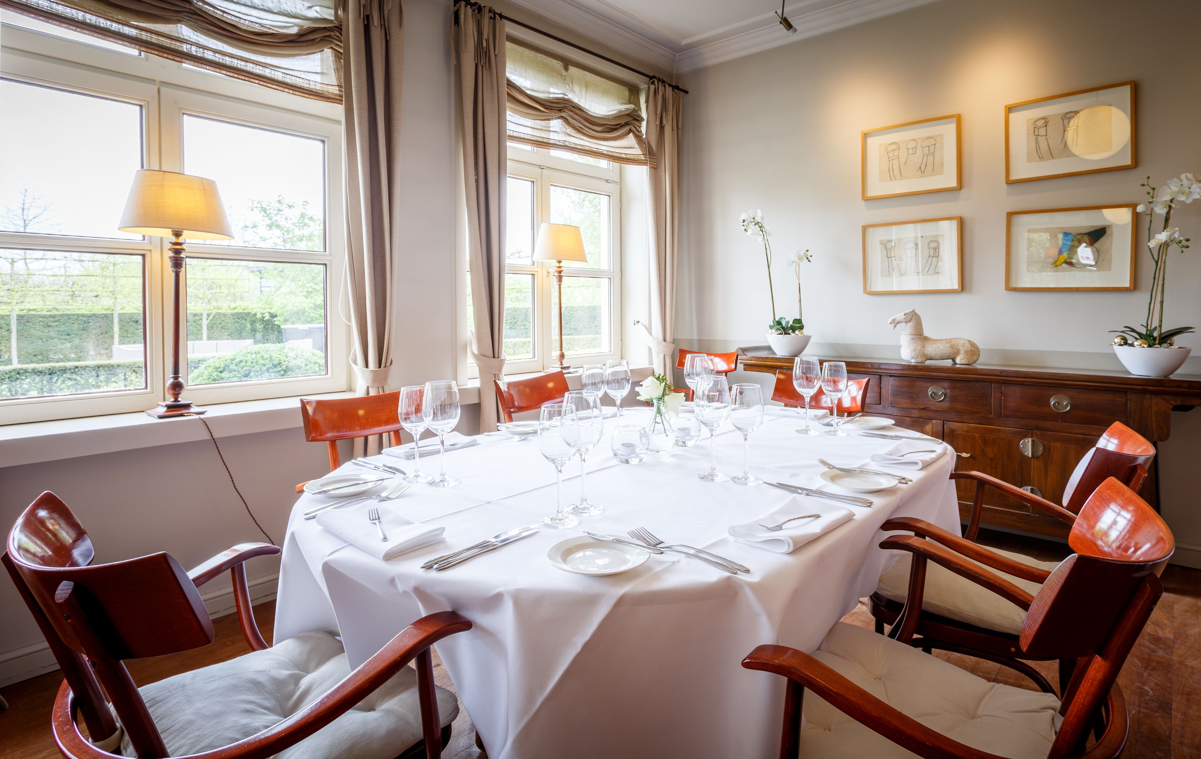 A dining room with a round table set for six, surrounded by wooden chairs.