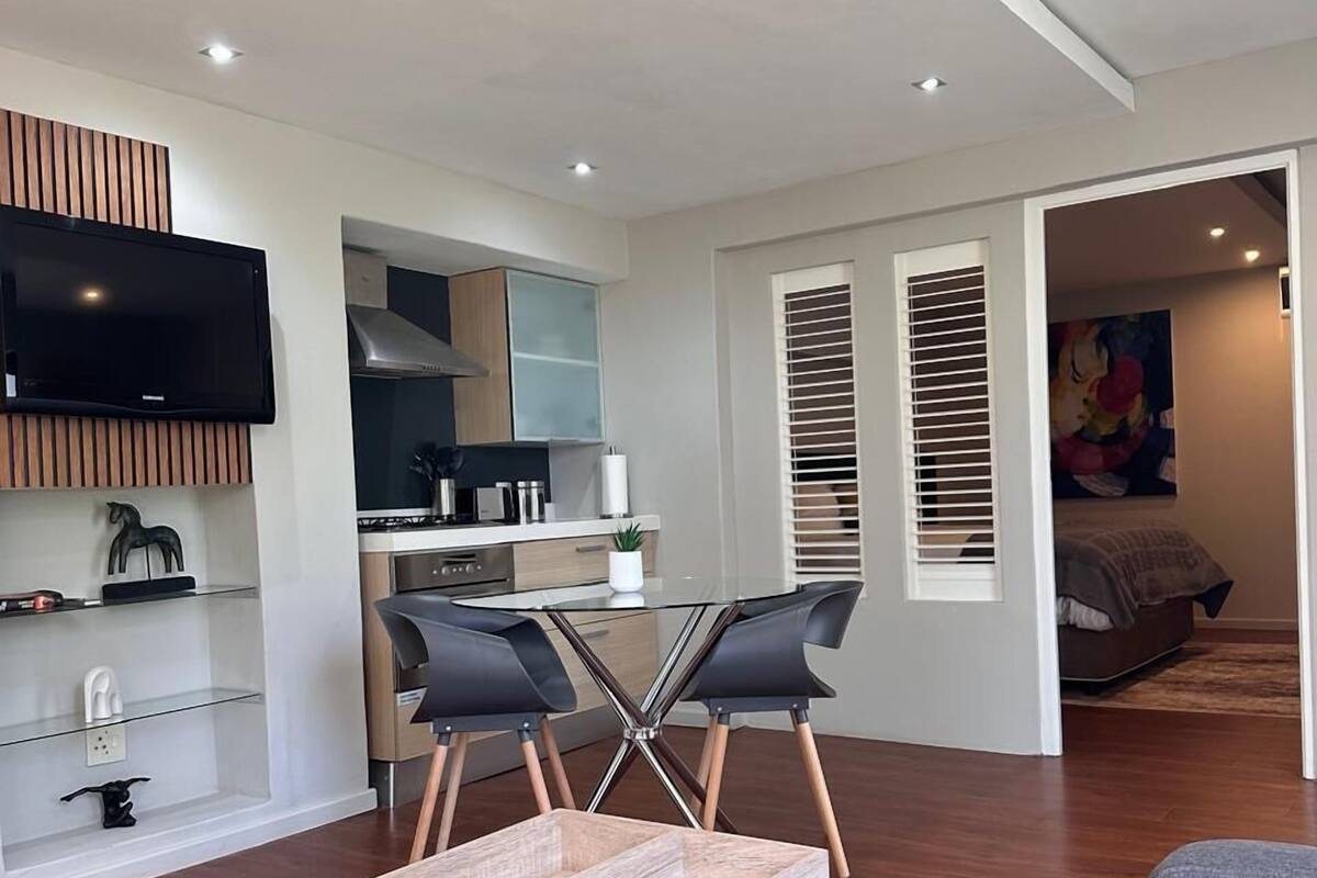 A modern living room with a wooden coffee table, grey sofa, and a dining area with a glass table and black chairs.