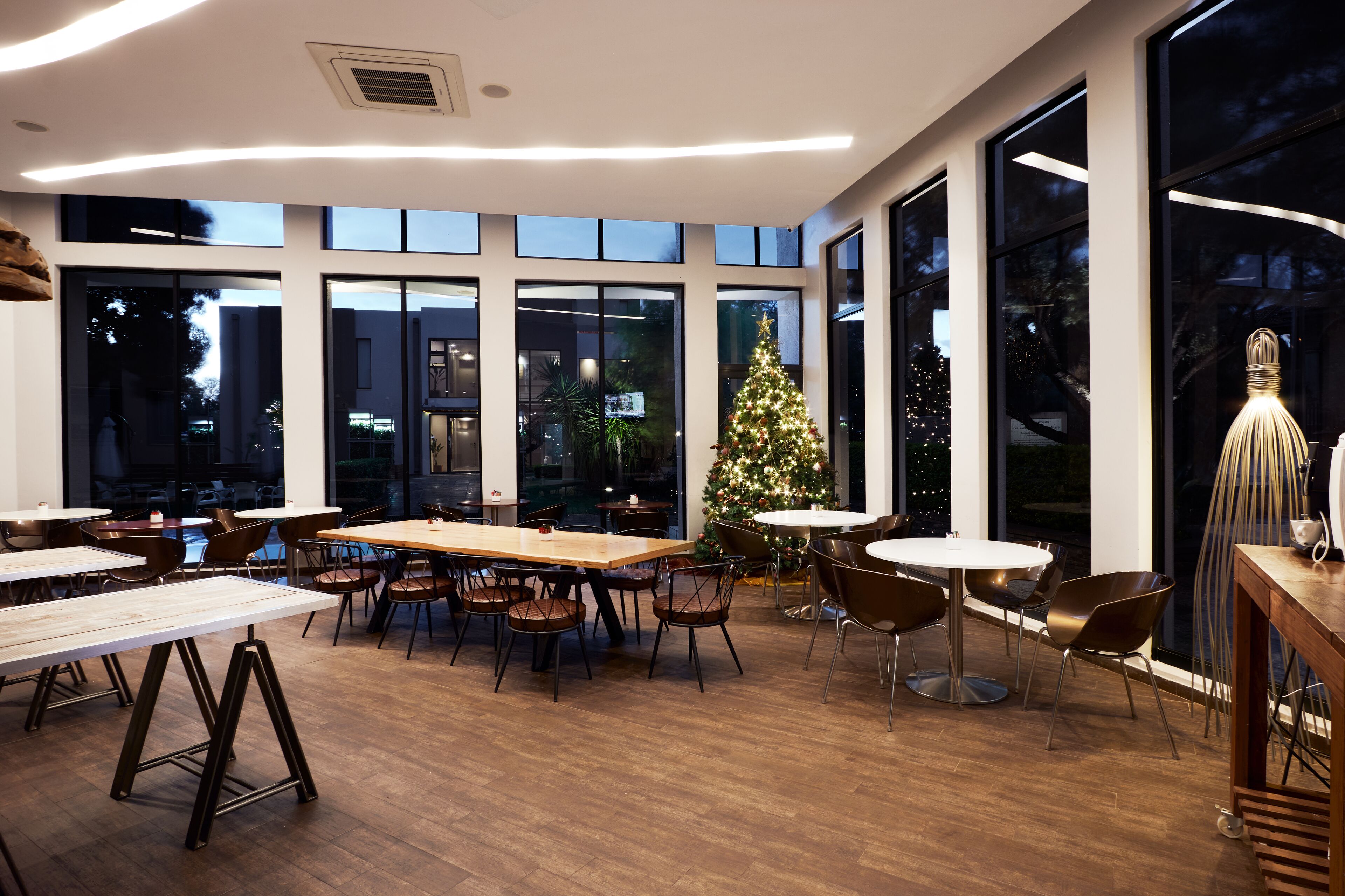 Un espace de restauration intérieur moderne, doté de grandes fenêtres, d’un sapin de Noël et de différents types de sièges.