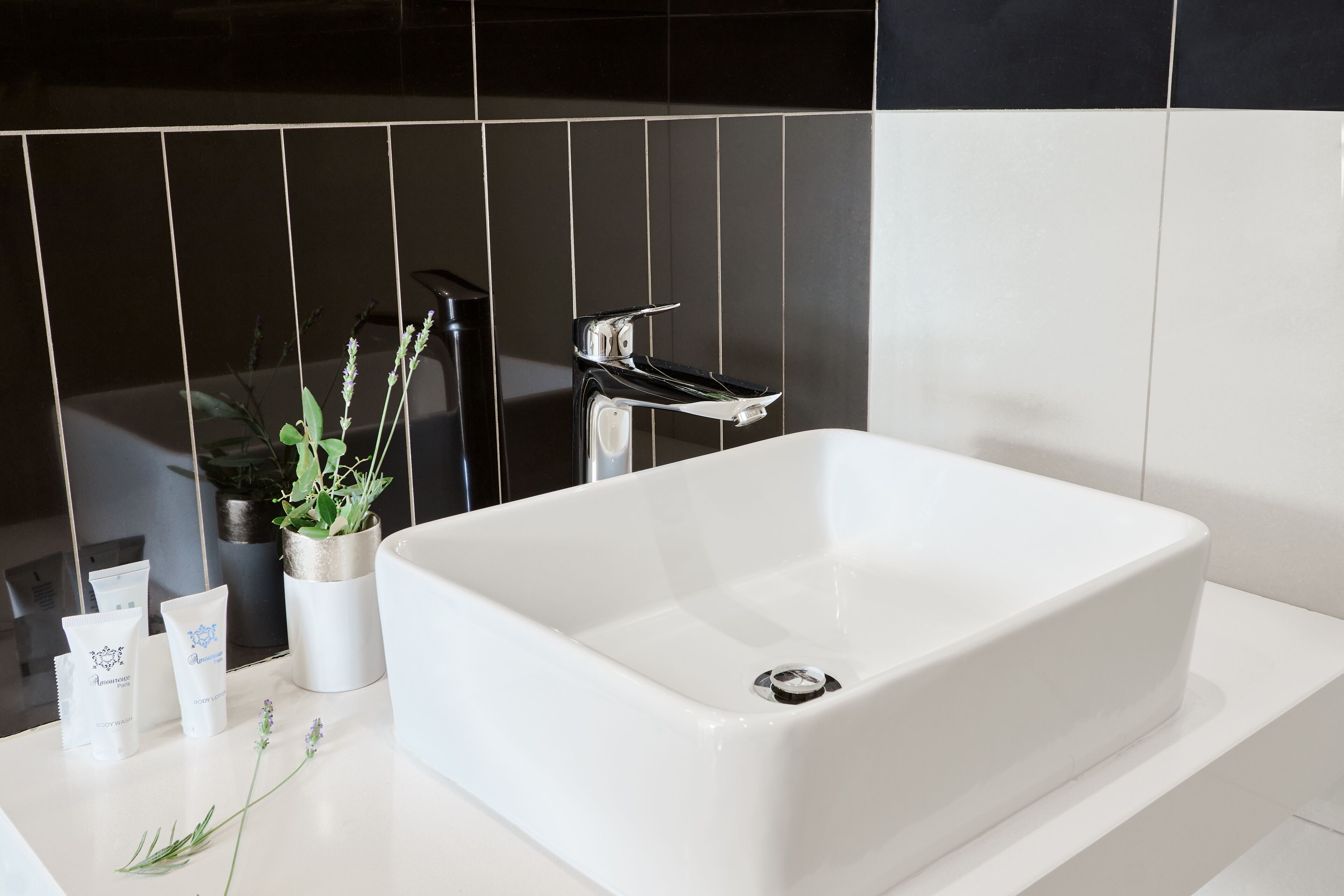 Een moderne badkamer met een wit wastafelmeubel, zwart-wit betegeling, een potplant en toiletartikelen op het aanrecht.