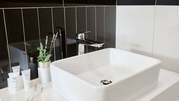 Une salle de bain moderne avec un lavabo blanc, des carreaux noirs et blancs, une plante en pot et des articles de toilette posés sur le comptoir.