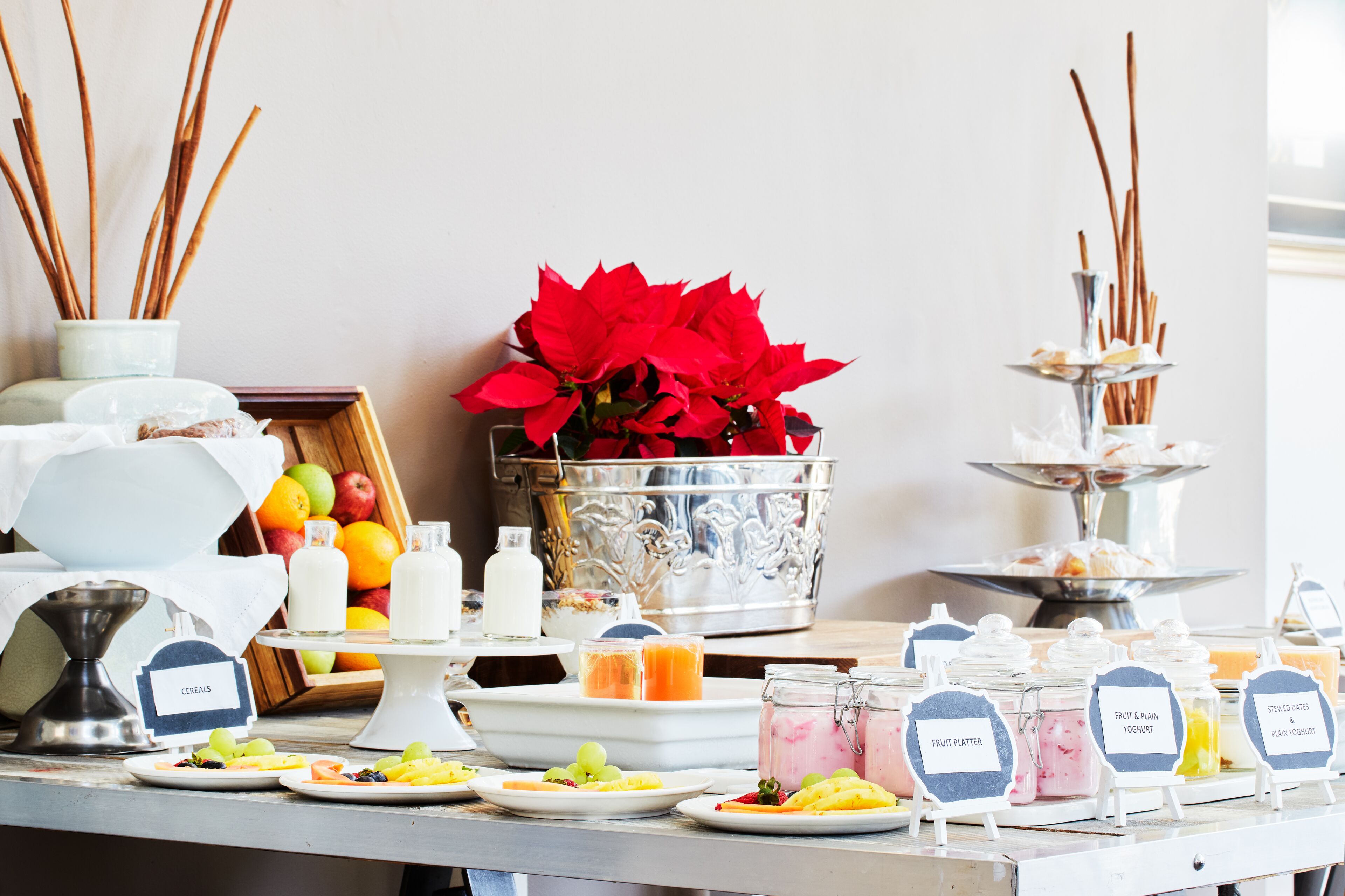 A breakfast buffet with labeled food stations including cereals, fruit platter, and fruit & plain yogurt.