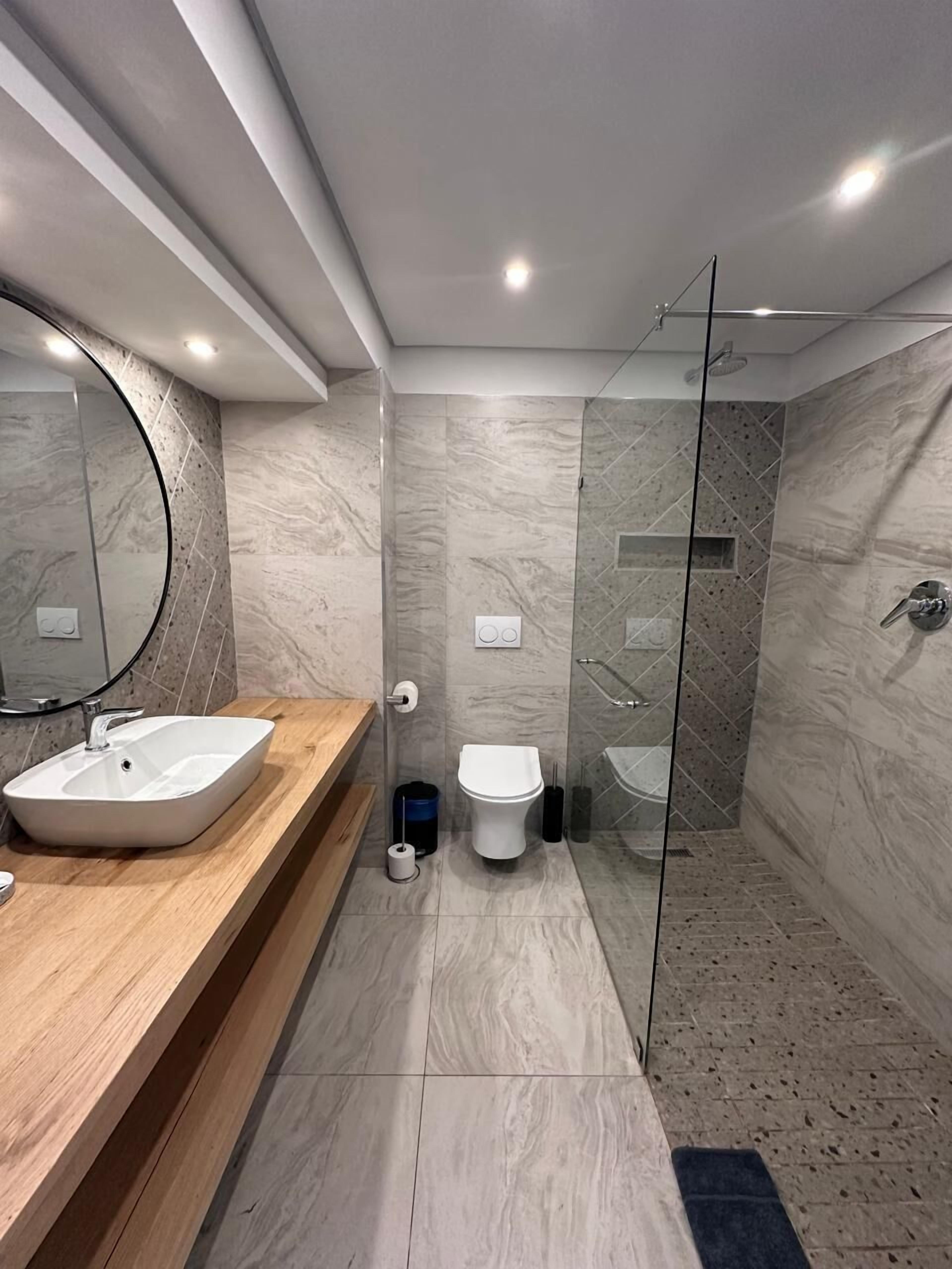 A modern bathroom with a marble vanity, a glass shower enclosure, and a toilet.