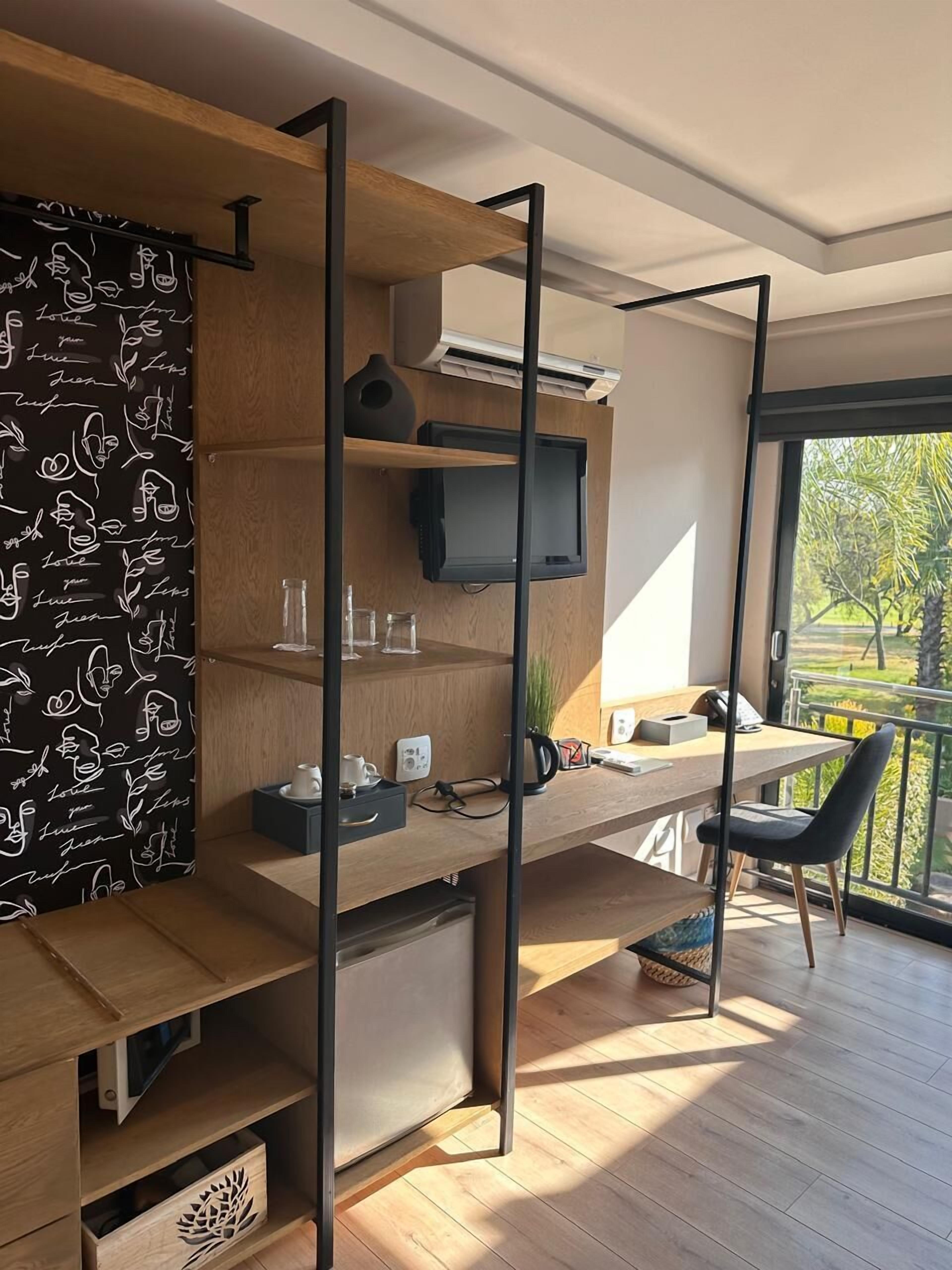 A modern home office with a wooden desk, a television, and a view of a garden through a large window.