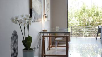 Una sala de estar moderna con una mesa de vidrio, una orquídea en maceta y un ventilador. Hay un comedor con una mesa y sillas de madera, y un balcón con vista a árboles.