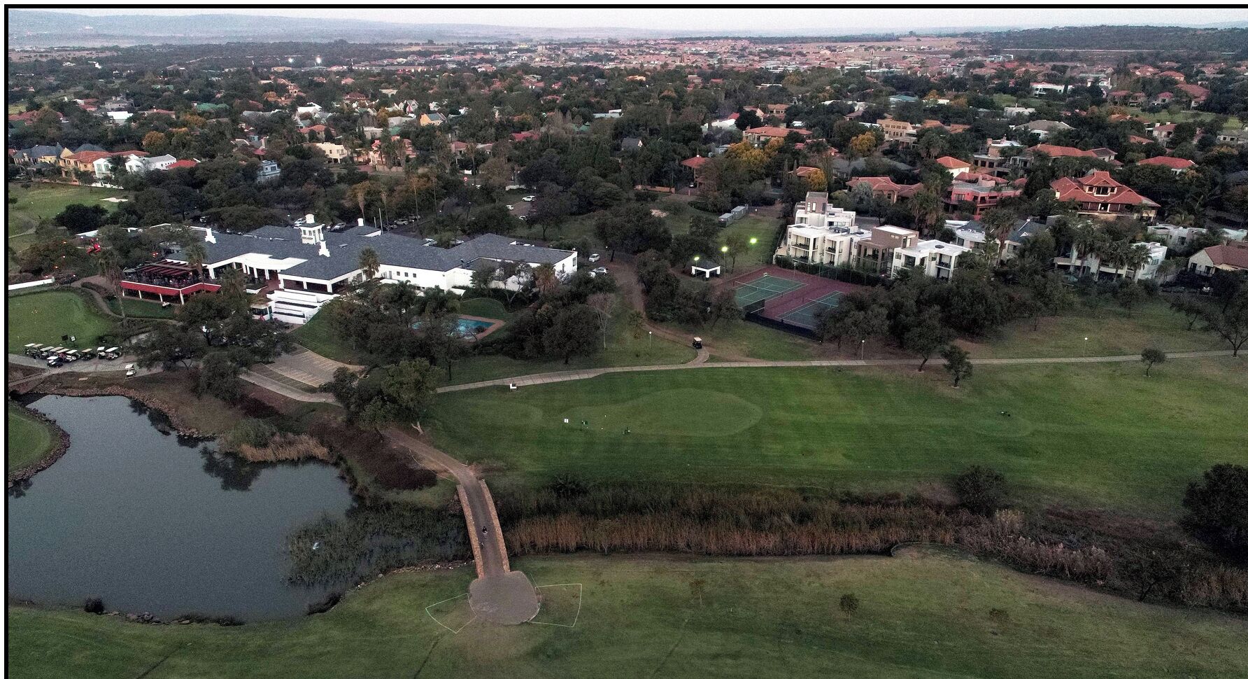 Vista aérea de una zona residencial con casas, un edificio blanco grande y un estanque.