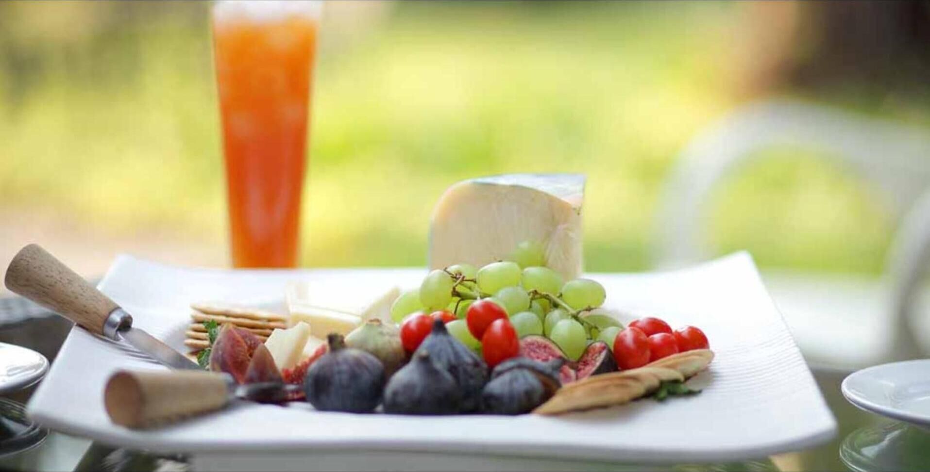 A cheese platter with grapes, tomatoes, and crackers on a white plate.