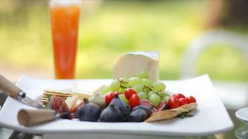 A cheese platter with grapes, tomatoes, and crackers on a white plate.
