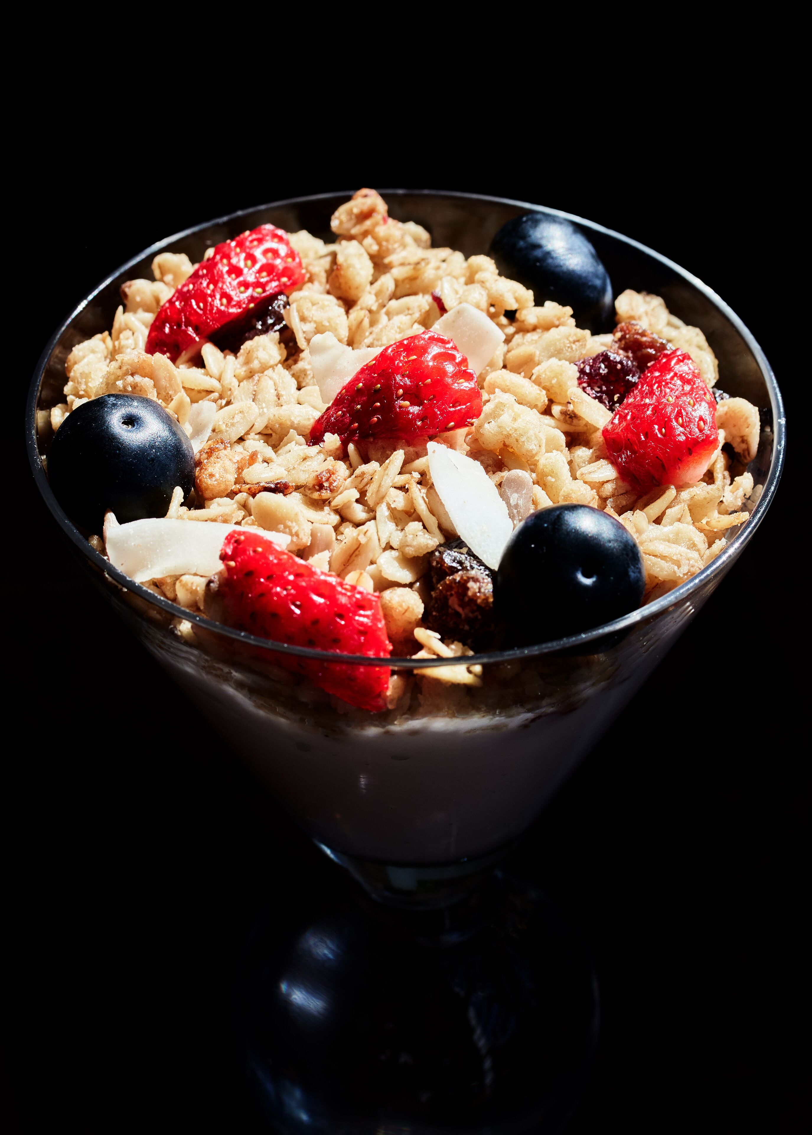 A bowl of cereal with strawberries, blueberries, and almonds.