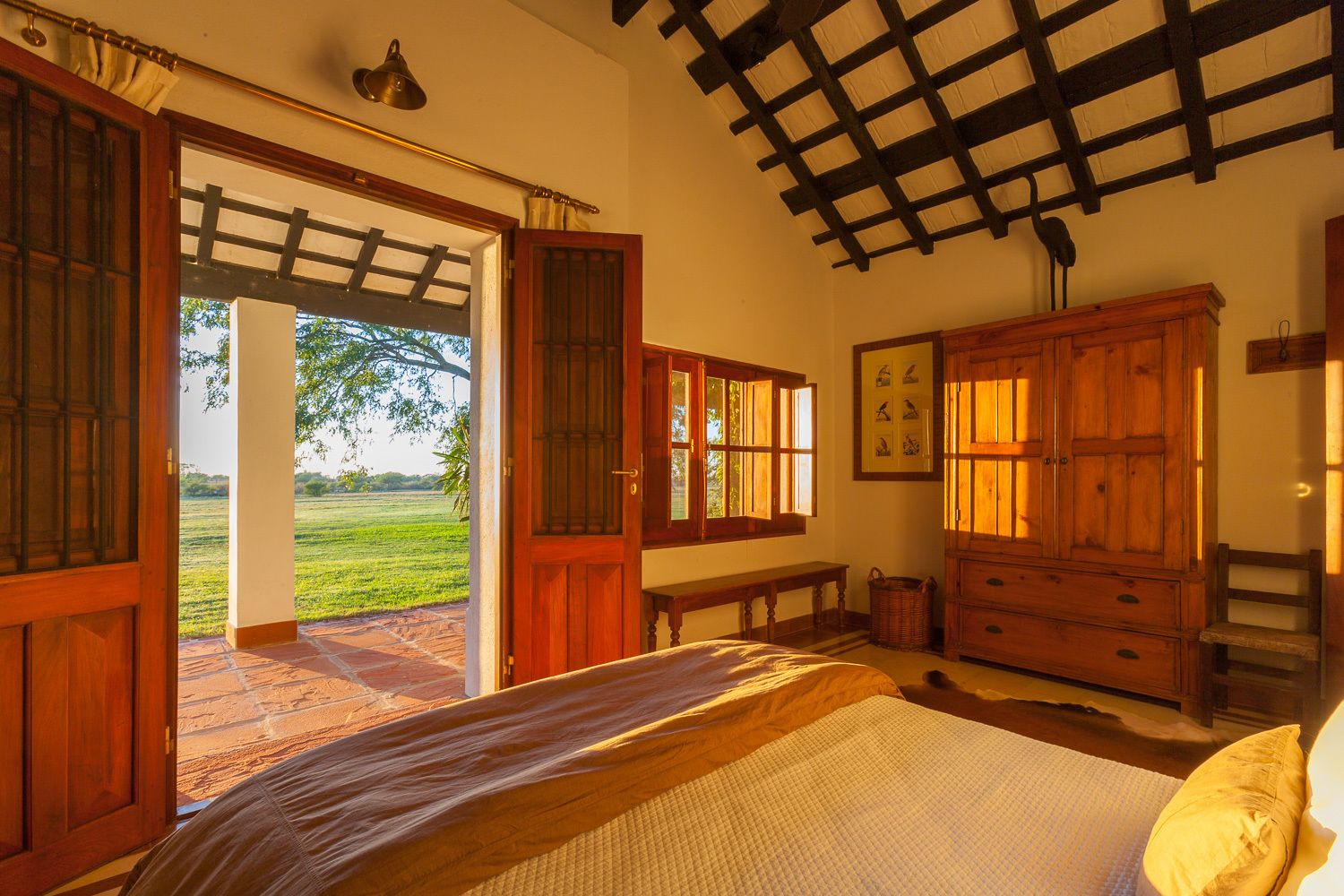 A bedroom with a bed, wooden wardrobe, and a view of a green field through open doors.