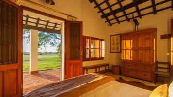 A bedroom with a bed, wooden wardrobe, and a view of a green field through open doors.