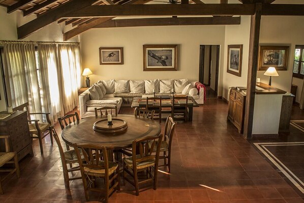 Amplia sala de estar con una mesa redonda de madera y sillas, un conjunto de sofás y cuadros en las paredes.
