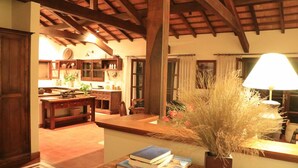 A cozy interior with a wooden ceiling, a kitchen area with cabinets, a dining table, and a lamp with dried plants.