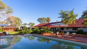 A swimming pool with lounge chairs and umbrellas, surrounded by greenery and buildings with red roofs.