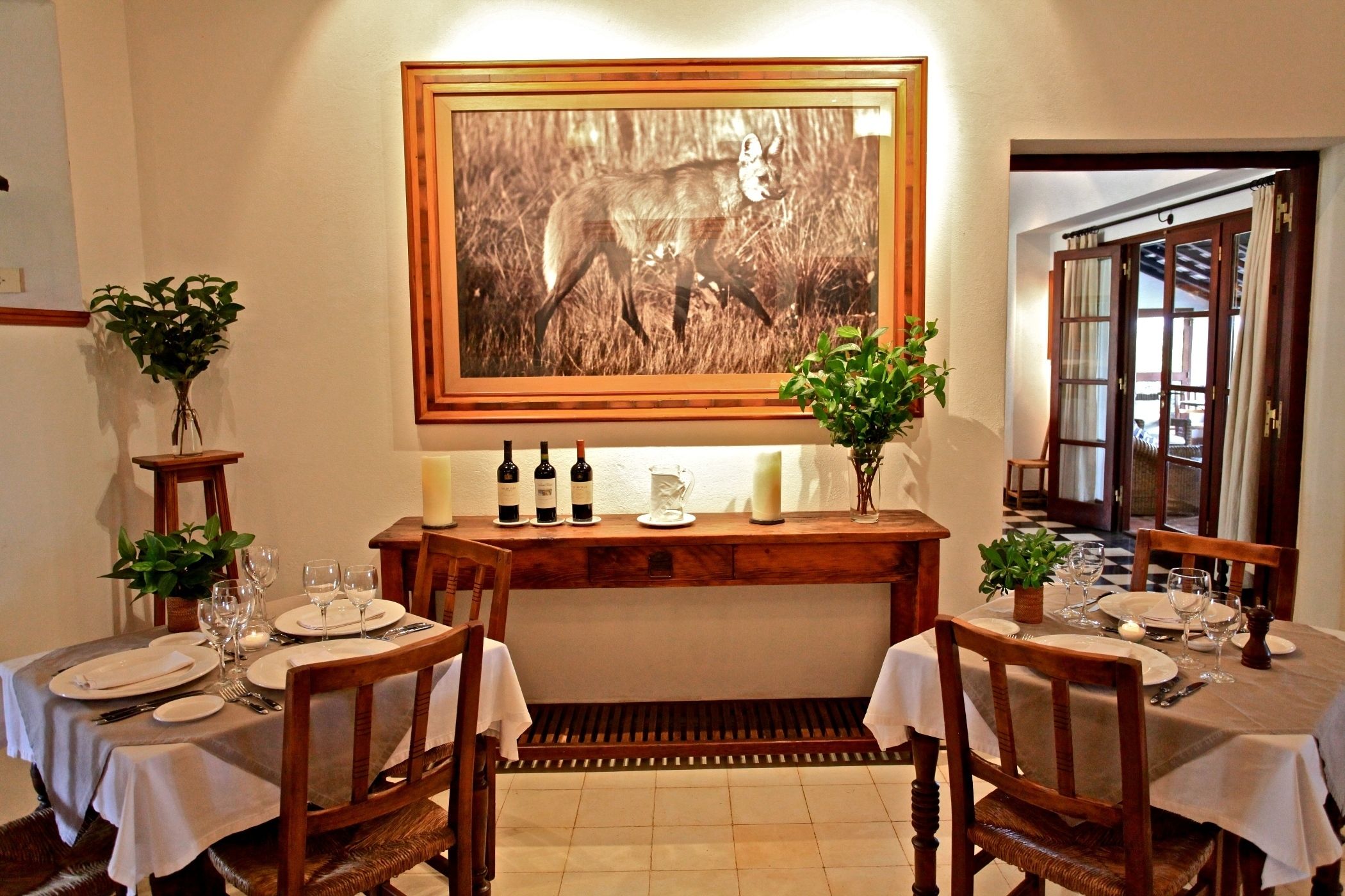 Zona pranzo con tavoli e sedie in legno, e una consolle centrale con bottiglie di vino e bicchieri.