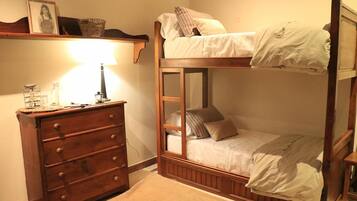 Een stapelbed met houten frame, een dressoir met lades, een lamp en een ingelijst foto aan de muur.