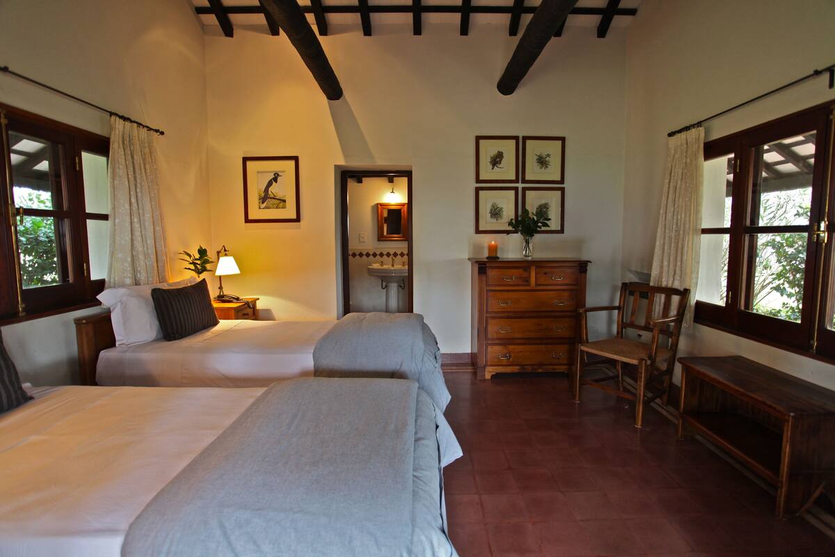 A bedroom with two beds, a wooden dresser, a chair, and a nightstand with a lamp.
