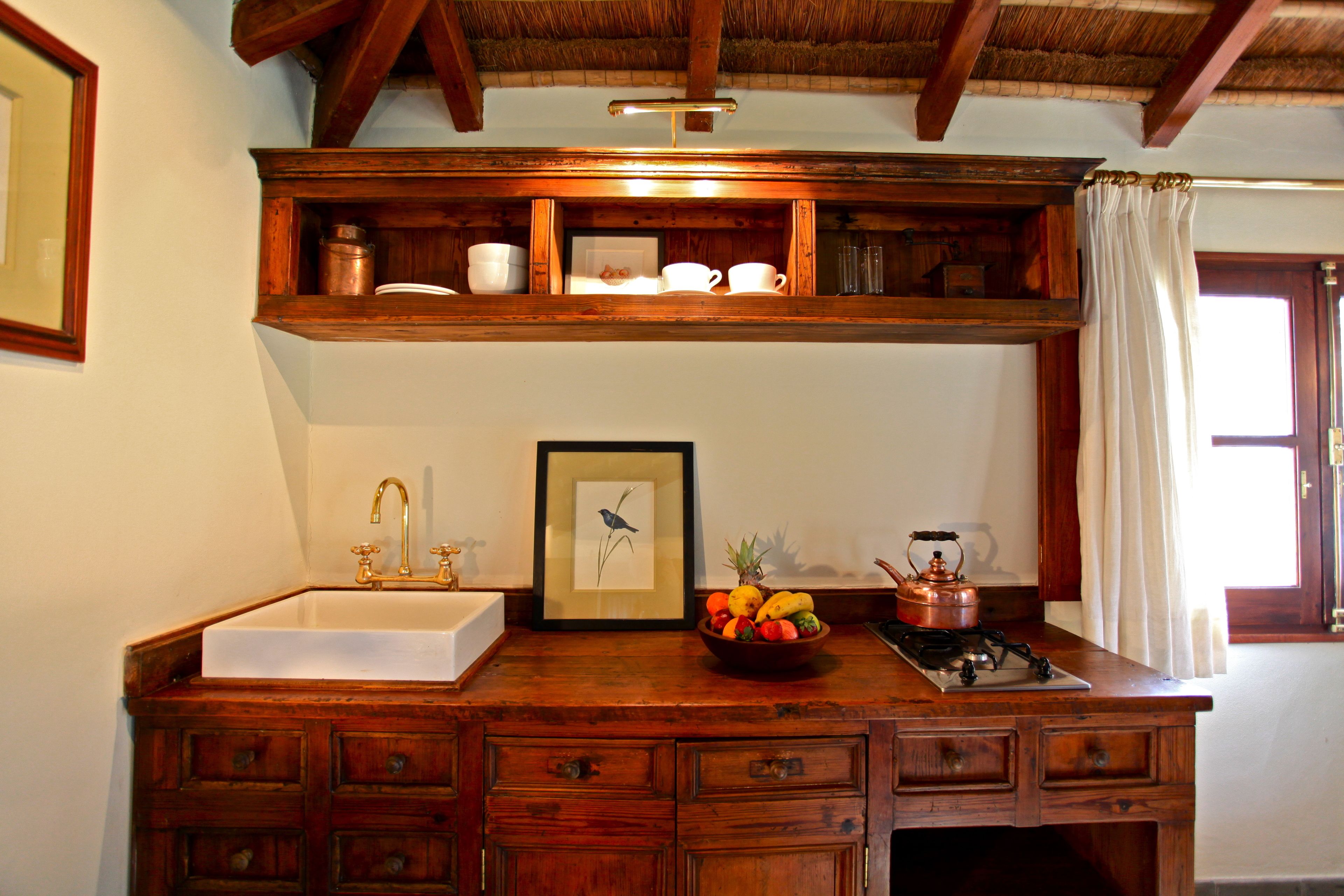 A wooden kitchen with a sink, a fruit bowl, a framed picture, and a stove.