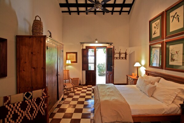 Una habitación con piso de cuadros, una cama con ropa blanca, muebles de madera y cuadros en la pared.