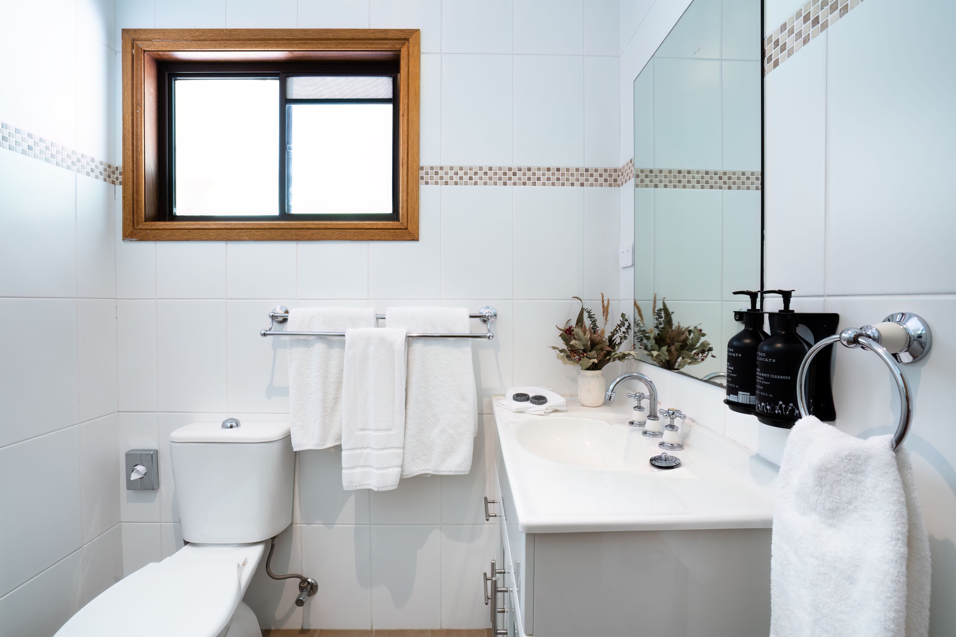 A modern bathroom with a toilet, sink, and a window above the toilet.