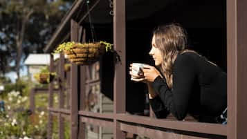 Una persona sentada junto a una ventana con una planta colgante, sosteniendo una taza.