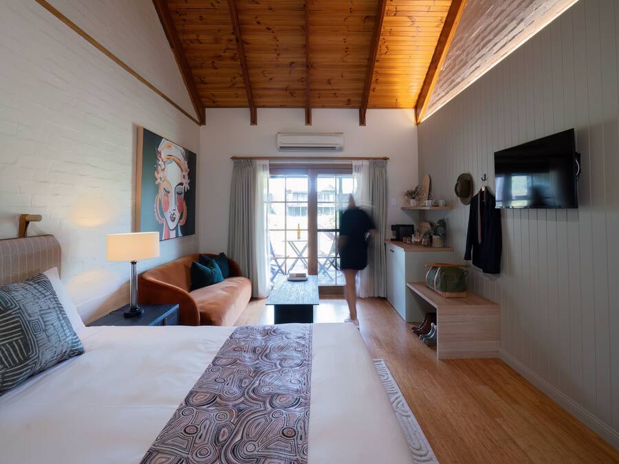 Una habitación de hotel con una cama grande, un sofá, un televisor y una ventana con cortinas.