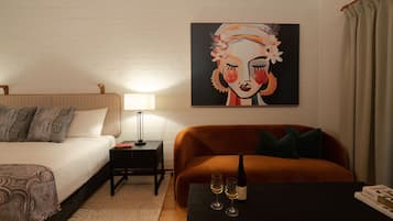 Una habitación de hotel moderna con una cama, un sofá, una mesita con una botella y vasos, y un cuadro en la pared.