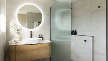 A modern bathroom with a round mirror, wooden vanity, and a glass shower enclosure.
