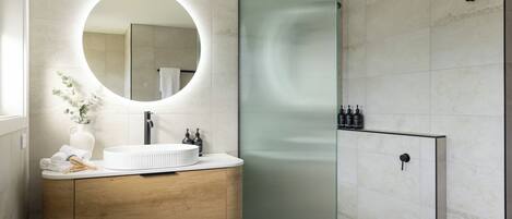 Une salle de bain moderne avec un grand miroir rond, un meuble-lavabo en bois et une cabine de douche en verre.