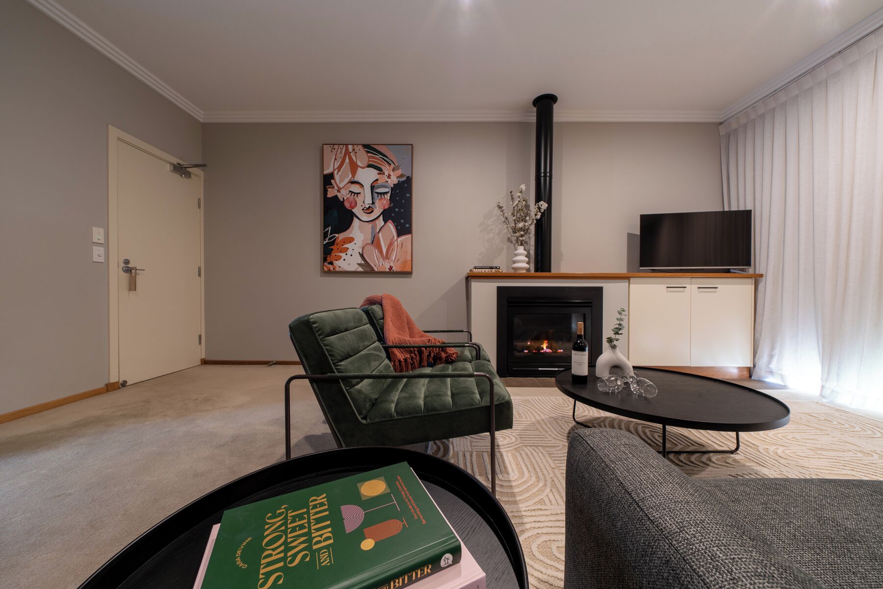A modern living room with a green sofa, a fireplace, a television, and a bookshelf with books.