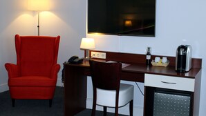 Ein Hotelzimmer mit einem roten Sessel, einem Schreibtisch mit Lampe, einem Fernseher, einer Kaffeemaschine und einem Minikühlschrank.