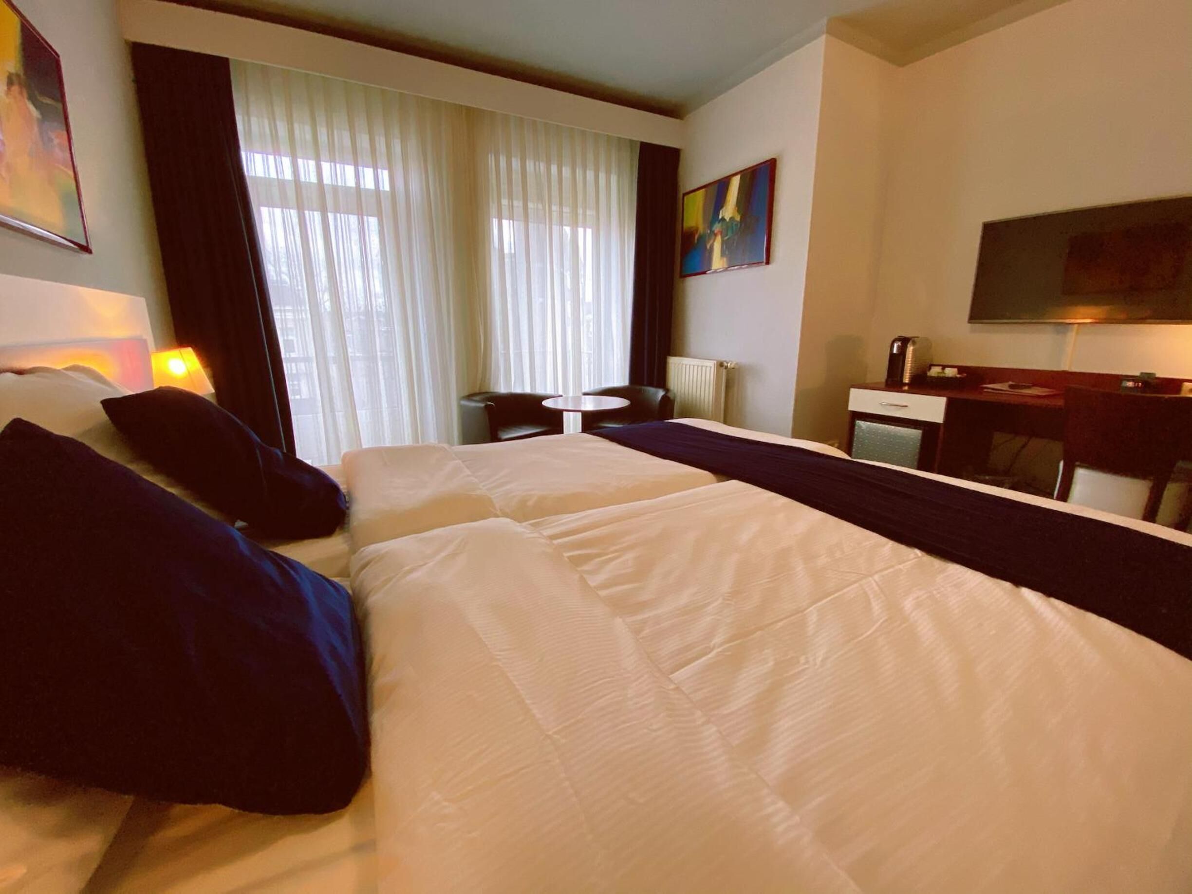 Ein Hotelzimmer mit zwei Betten, einem Schreibtisch, einem Stuhl, einem kleinen Tisch und einem Fernseher.
