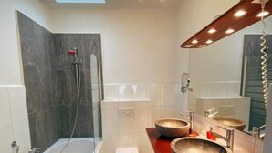 Ein modernes Badezimmer mit einer Badewanne, zwei Waschbecken mit Steinschalen, einer Toilette und einem Oberlicht über der Duschfläche.