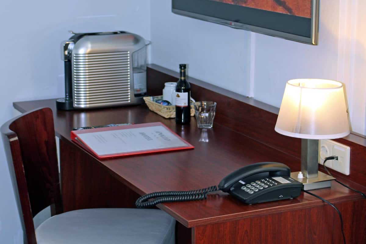 A hotel room with a wooden desk, a telephone, a lamp, a framed picture on the wall, and a minibar.