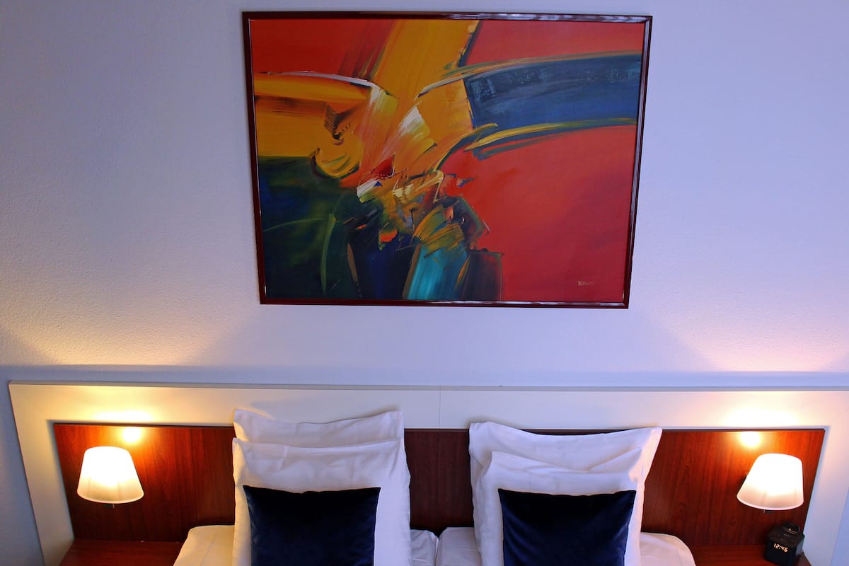 A hotel room with a bed, two bedside lamps, and a large abstract painting on the wall.