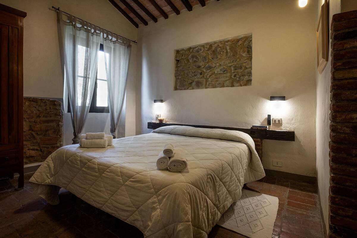 A bedroom with a large bed, stone wall, and a stone fireplace.