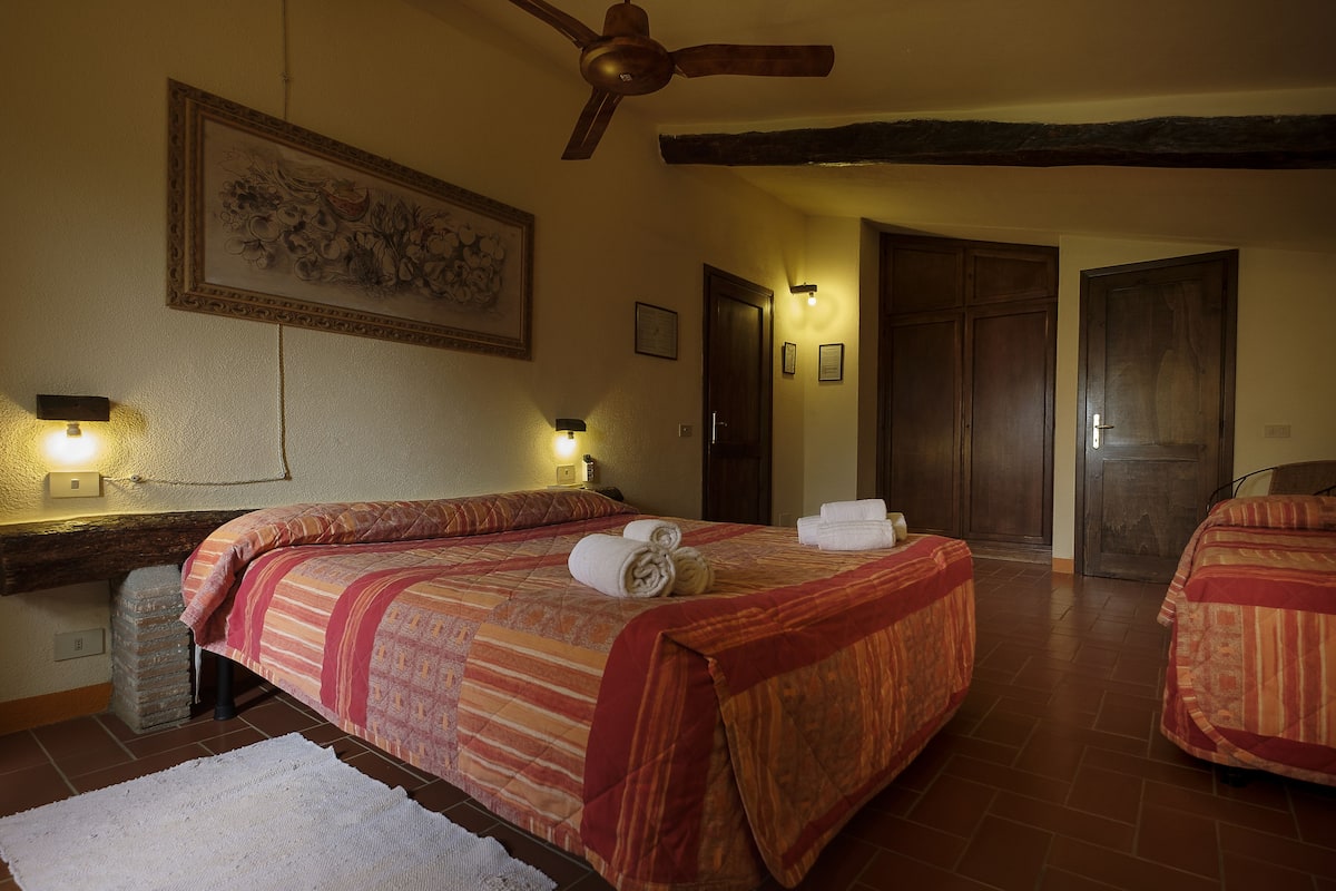 A hotel room with a large bed, a ceiling fan, a painting on the wall, and two doors.