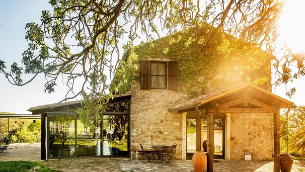 A stone house with a glass door, a patio with a table and chairs, and a garden area. - Az Agrituristica Bio Le Macchie Alte (Manciano)
