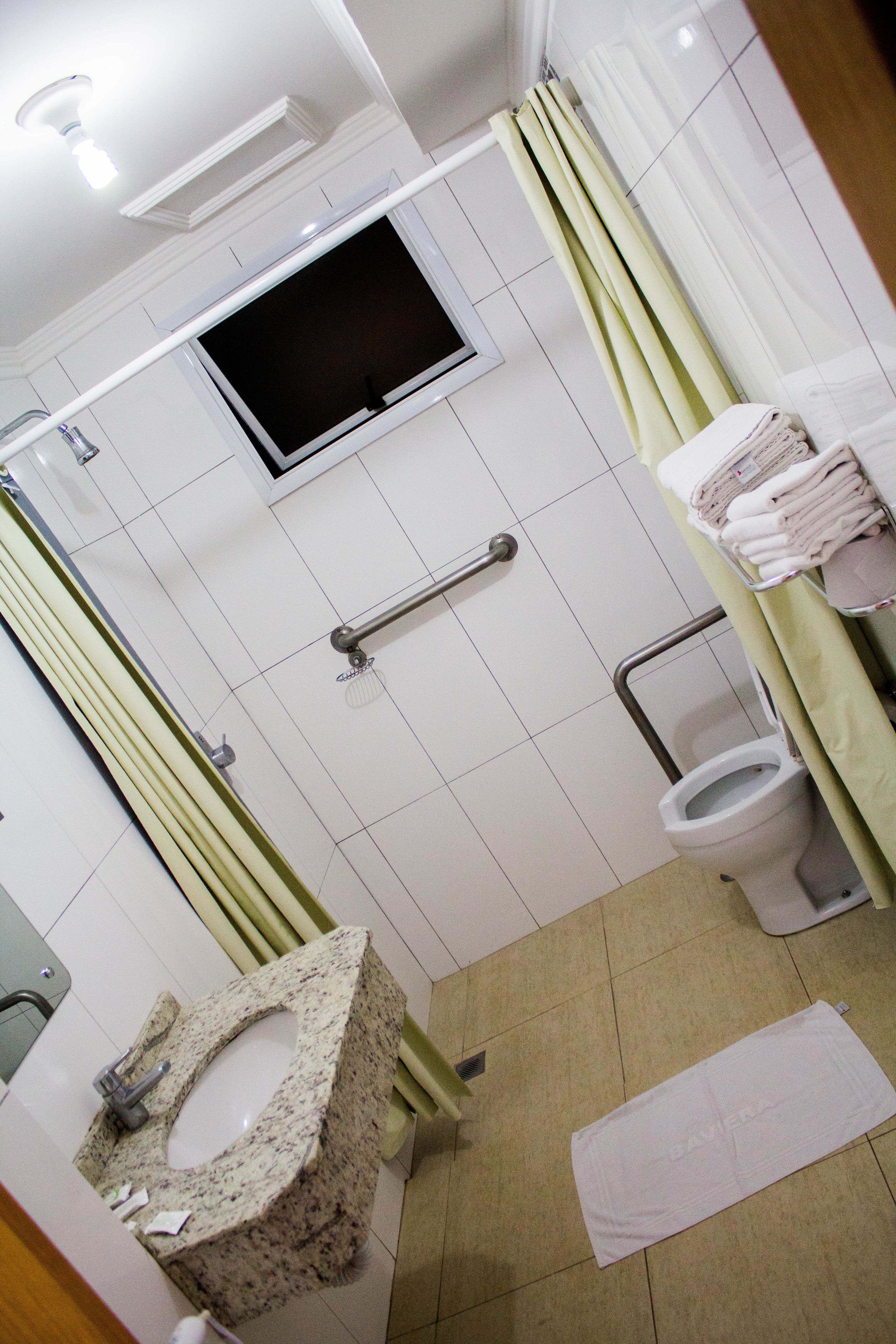 Un baño con lavamanos de granito, inodoro, ducha con puerta de cristal y televisor montado en la pared.