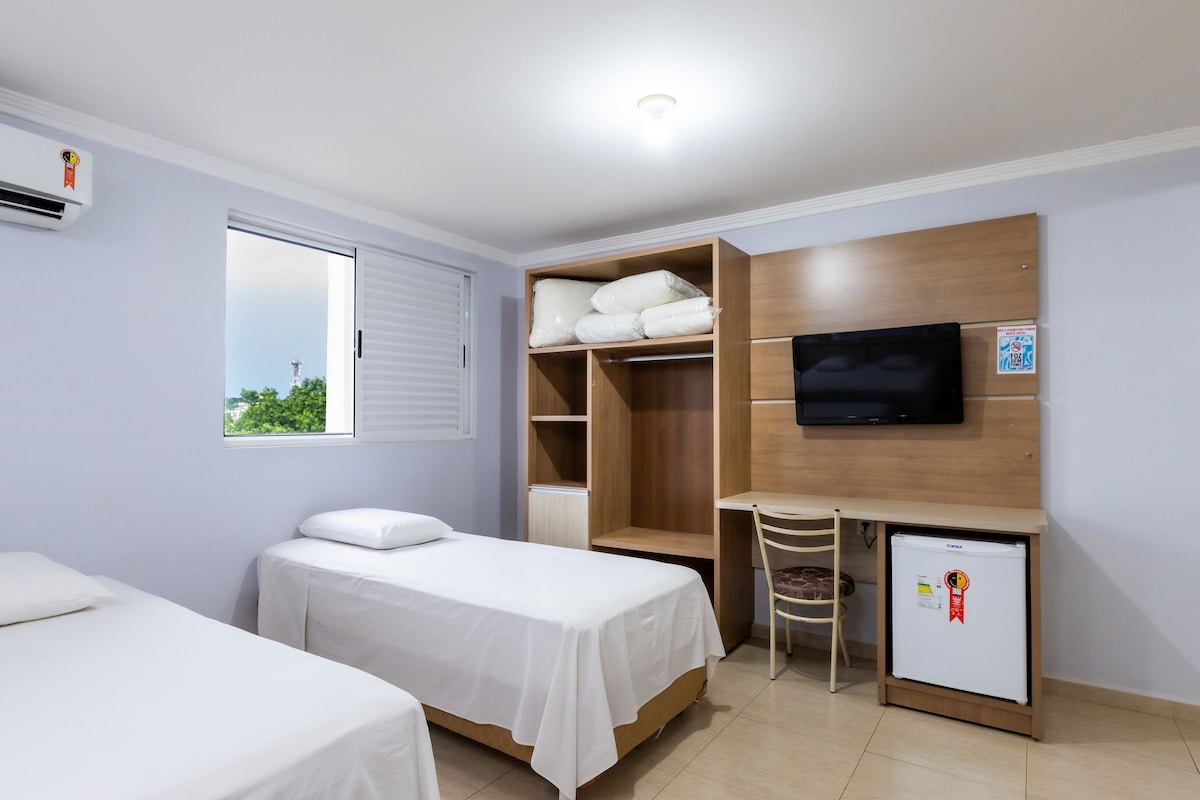 A room with two beds, a desk, a TV, and a mini-fridge.
