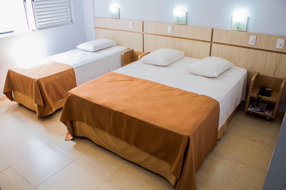 Een hotelkamer met twee enkele bedden en een tweepersoonsbed, elk met een ander kleurend beddegoed.
