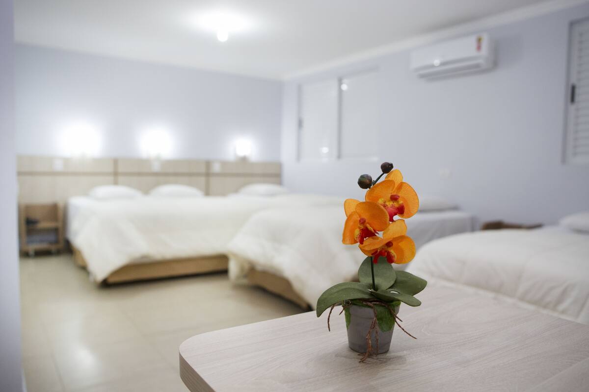 Een hotelkamer met een bed, een nachtkastje met een potorkidee en een witte airconditioner aan de muur.