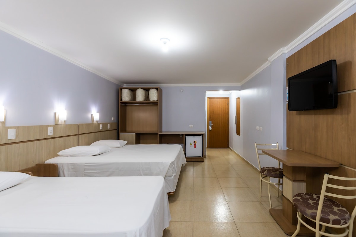 A hotel room with two beds, a desk, a chair, a television, and a refrigerator.