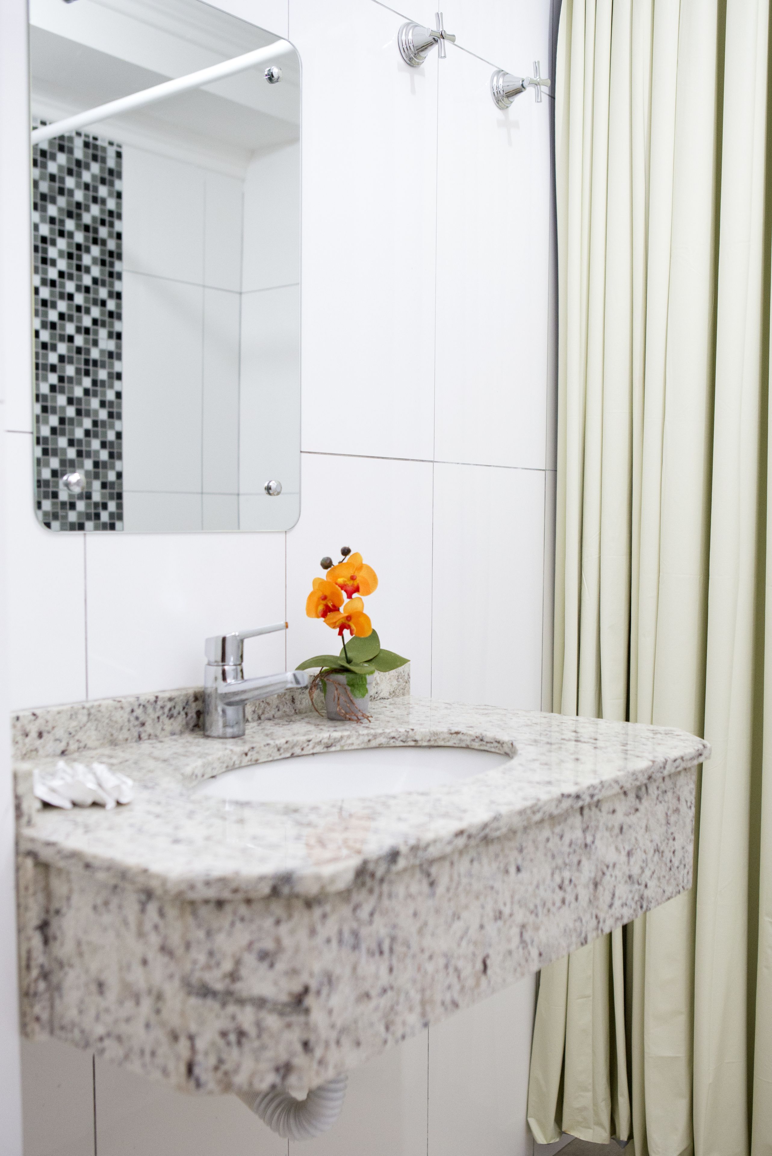 A bathroom with a white tiled wall, a sink with a marble countertop, a mirror, and a shower curtain.