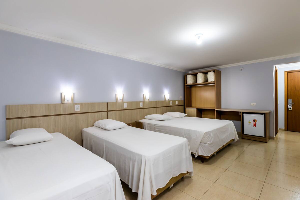 Een hotelkamer met vier eenpersoonsbedden, een klein bureau, een kledingkast en een koelkast.