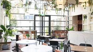 A modern cafe with round tables, black and orange chairs, and hanging plants.
