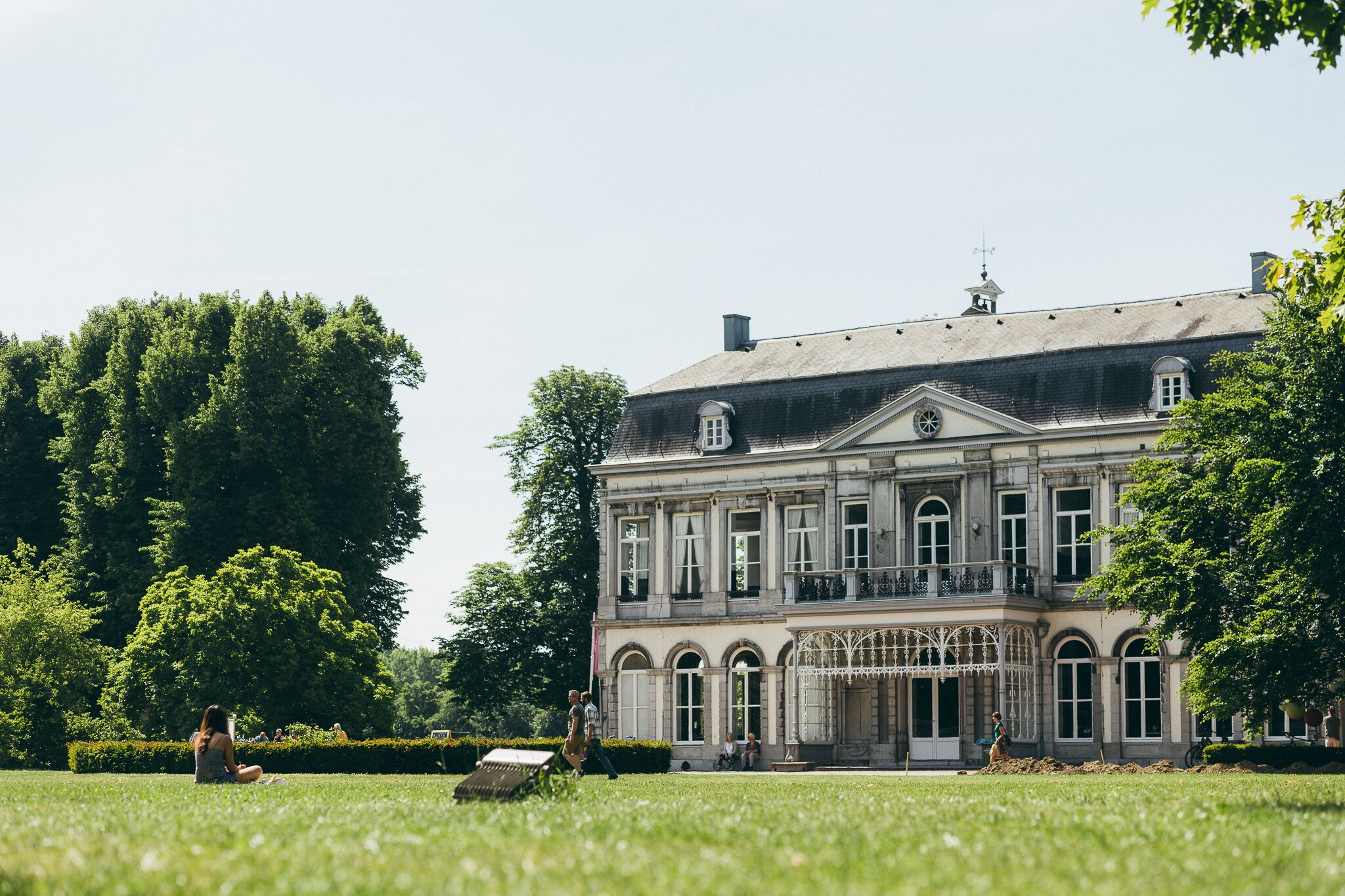 A large, historic building with multiple windows and a balcony, surrounded by lush greenery.